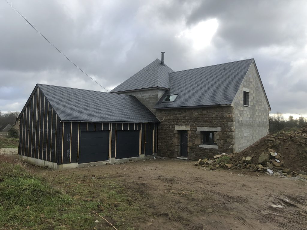 Chantier de construction d'une maison individuelle en pierre et parpaings avec extension de garage sous isolation extérieure.